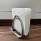 Metal stirrup-shaped napkin holder with white paper towels on a wooden surface.