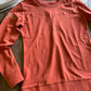 Coral-colored long-sleeve shirt with decorative elements on a wooden surface