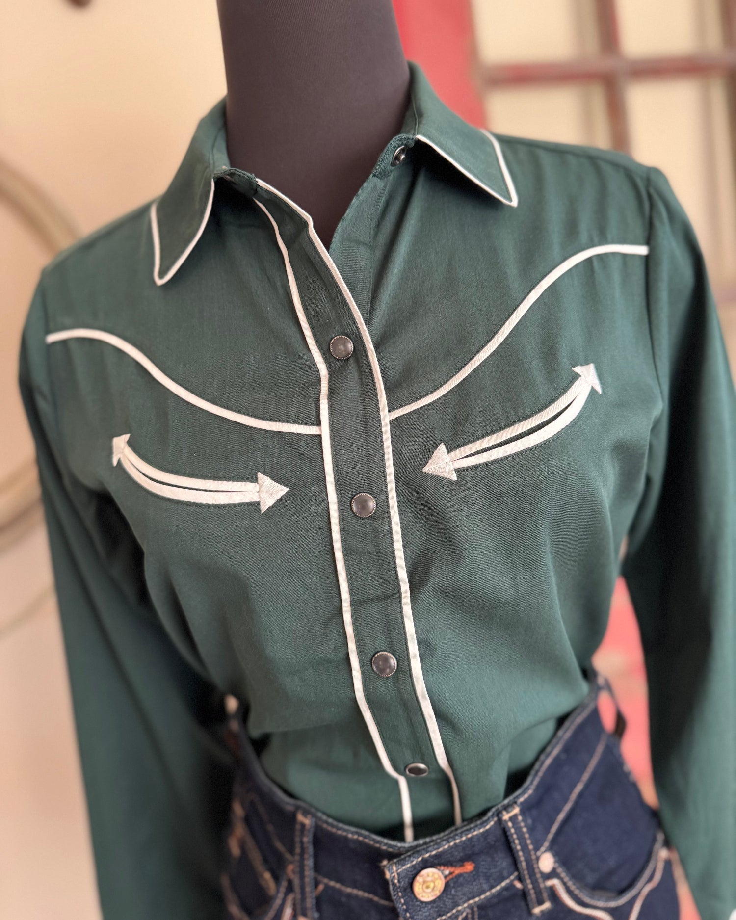 Green shirt with white stitching on a mannequin against a neutral background