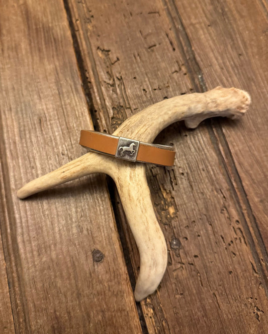 Brown leather cuff with a silver clasp on a deer antler, placed on a wooden surface.