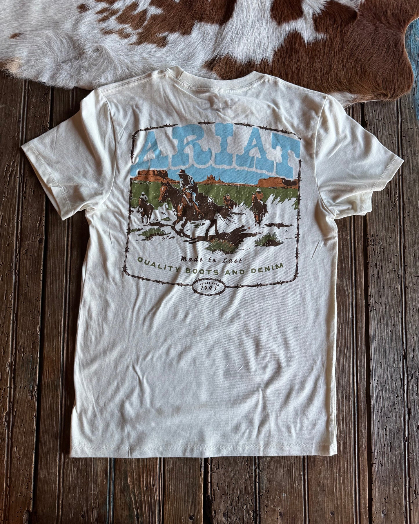 White t-shirt with graphic design on a wooden surface with a cowhide rug in the background