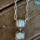 A silver link chain necklace with two stacked rectangular cabochon gemstone pendants, displayed on a rustic dark wood surface.