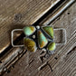 Silver twilly slide with green gemstones on a wooden surface