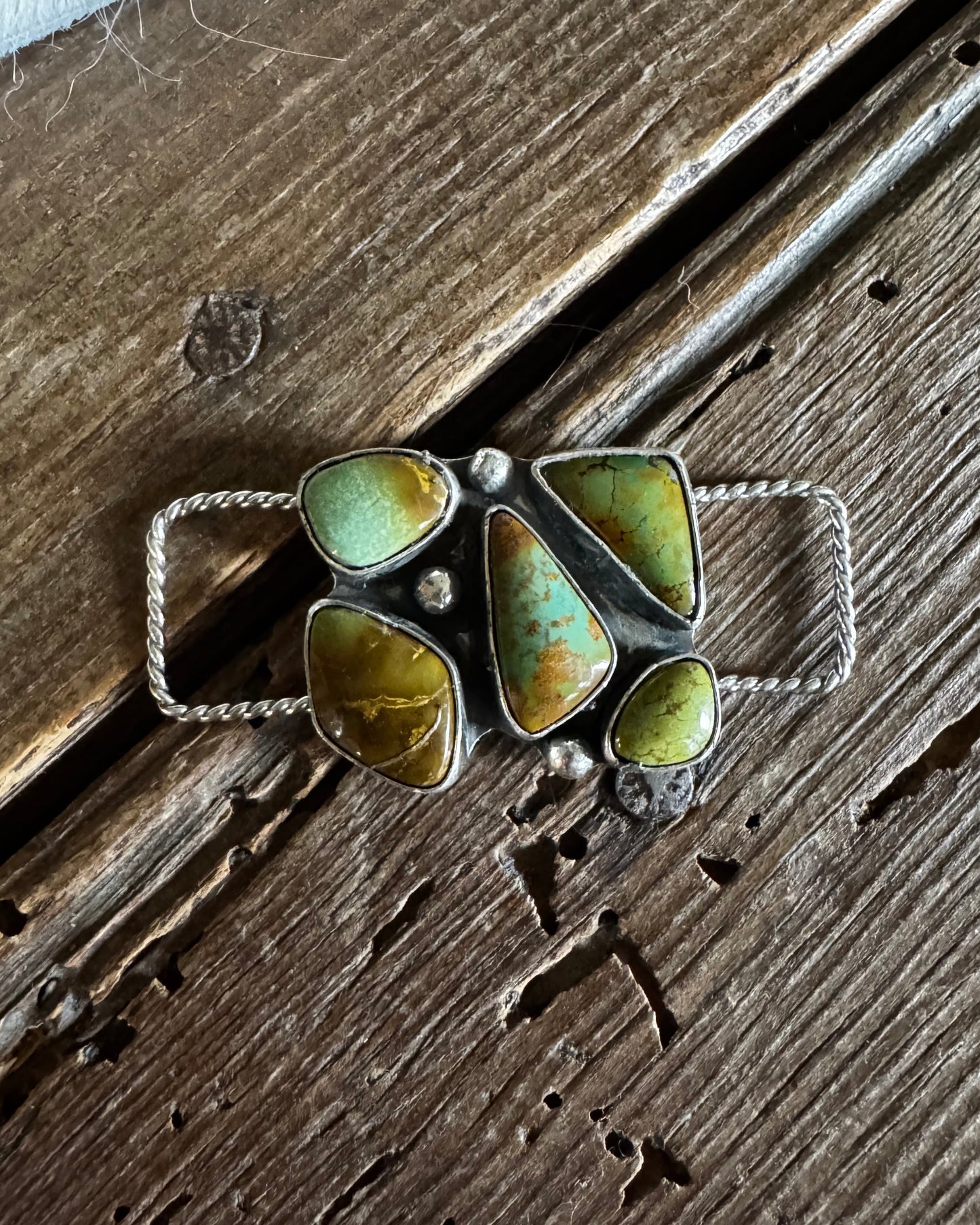 Silver twilly slide with green gemstones on a wooden surface