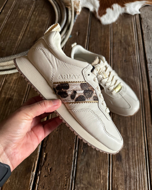 Beige sneaker with leopard print accents held by a hand against a wooden background