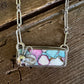 A rectangular pendant necklace with a colorful marbled inlay of turquoise, pink, and white, set in silver with a small butterfly charm, displayed on a rustic wooden surface.
