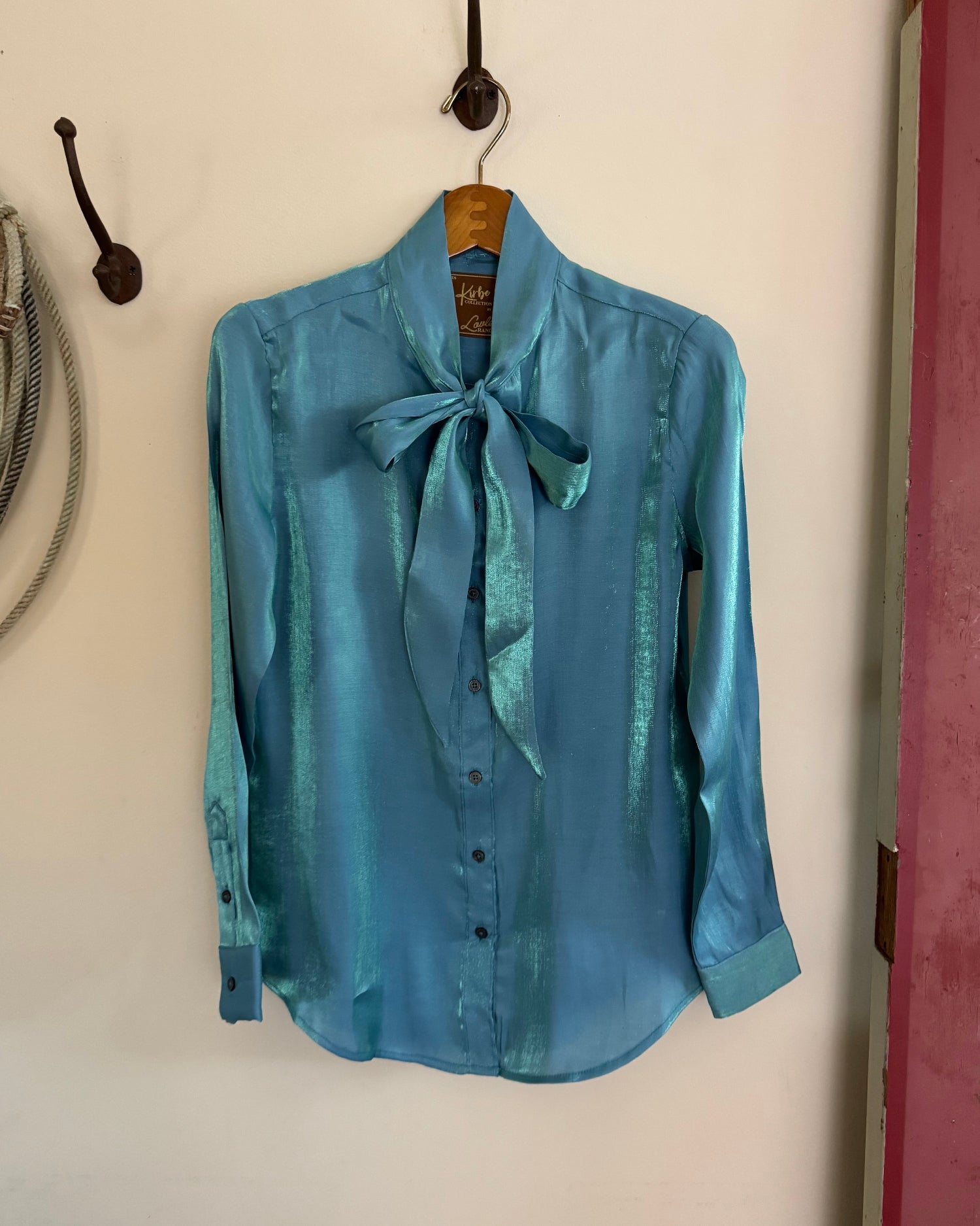 Blue shirt with a bow tie hanging on a hook against a white wall.