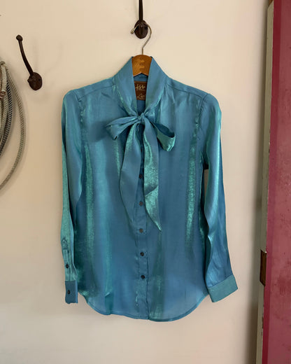 Blue shirt with a bow tie hanging on a hook against a white wall.