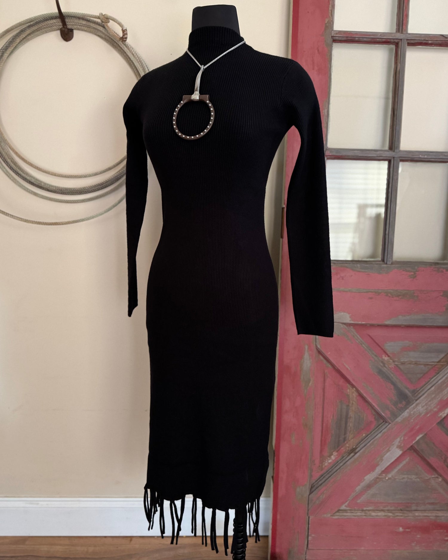 black sweater dress with fringe in front of a white wall with a rope and old door