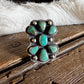 A silver ring with turquoise stones, displayed on a rustic wooden surface with a white fur trim and a blurred background.