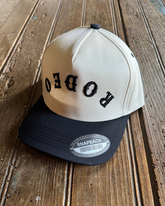 Beige and black cap with 'RODEO' text on a wooden surface
