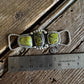 Silver twilly slide with green stones on a wooden surface with a ruler for scale.