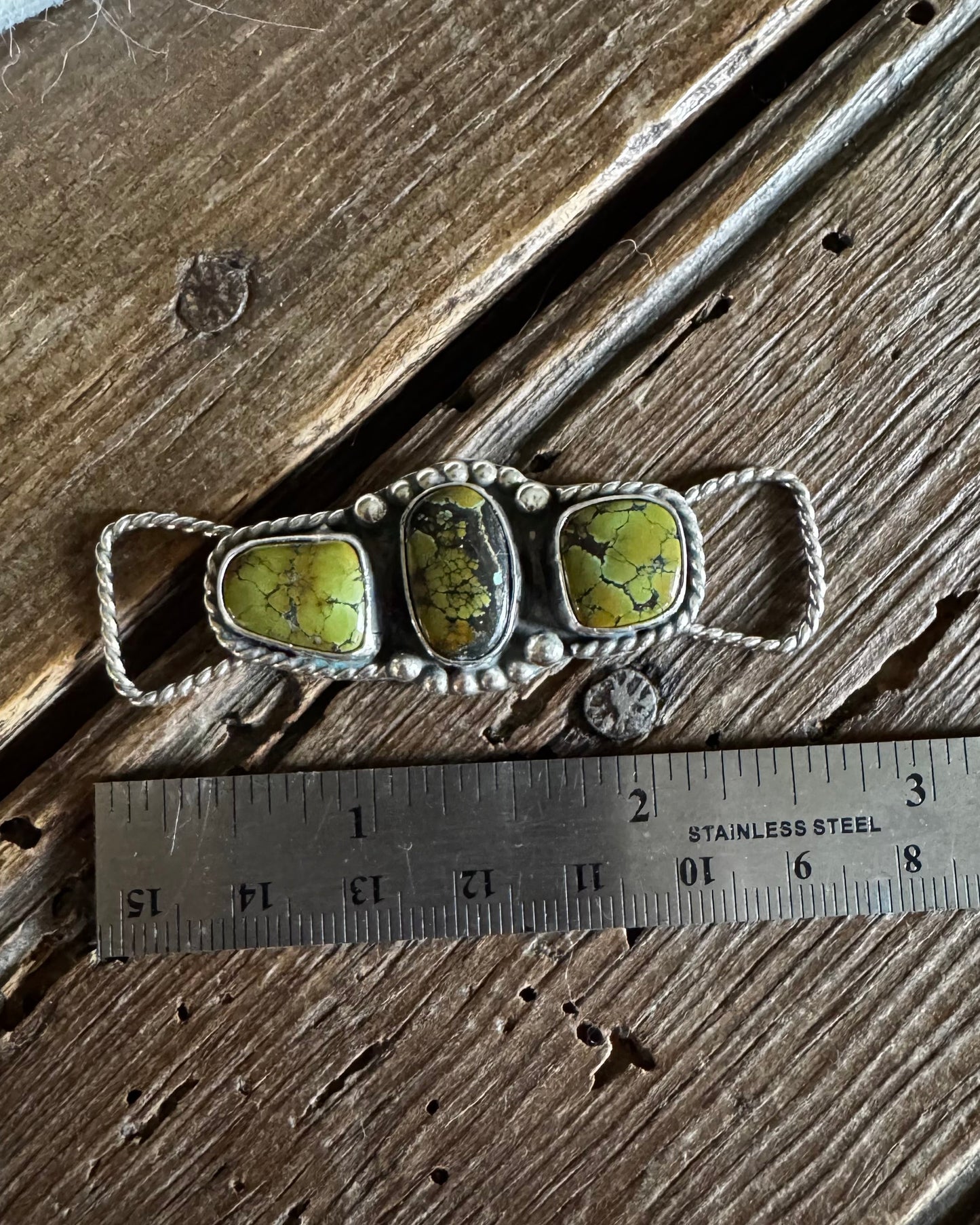 Silver twilly slide with green stones on a wooden surface with a ruler for scale.