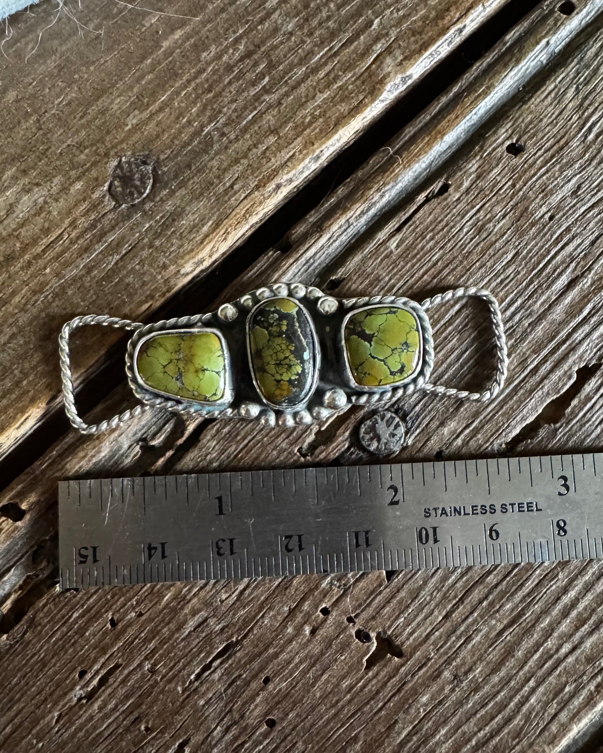 Silver twilly slide with green stones on a wooden surface with a ruler for scale.