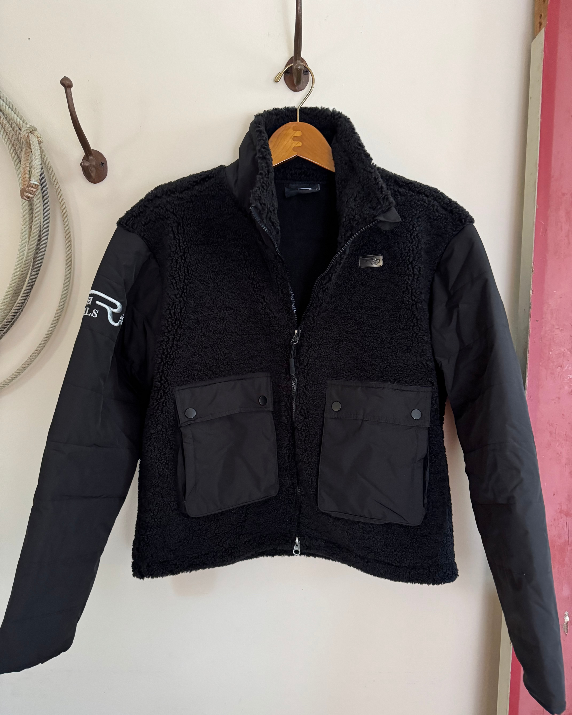 Black jacket with a brand logo hanging on a hook against a white wall.