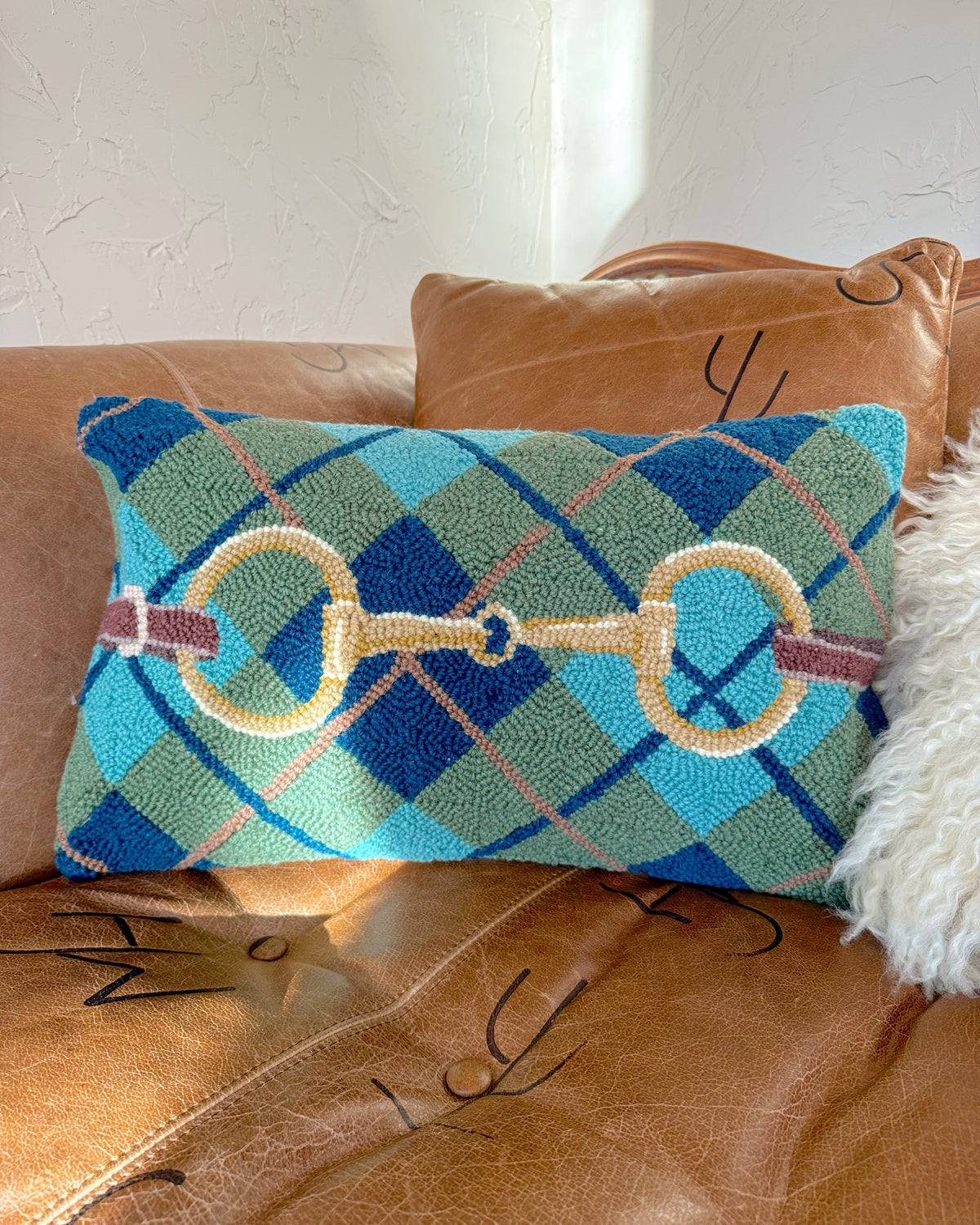 Decorative pillow with plaid pattern and equestrian design on a brown leather couch.