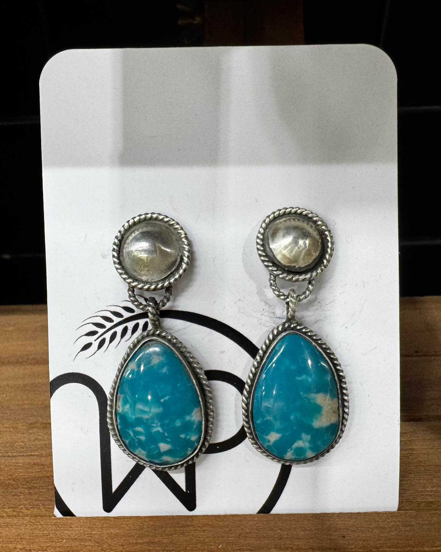 Pair of turquoise teardrop earrings on a white card with black designs, placed on a wooden surface.