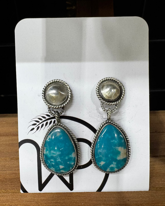 Pair of turquoise teardrop earrings on a white card with black designs, placed on a wooden surface.