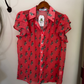 A red short-sleeve button-up blouse with a green cactus print, hanging on a wooden hanger against a white wall.
