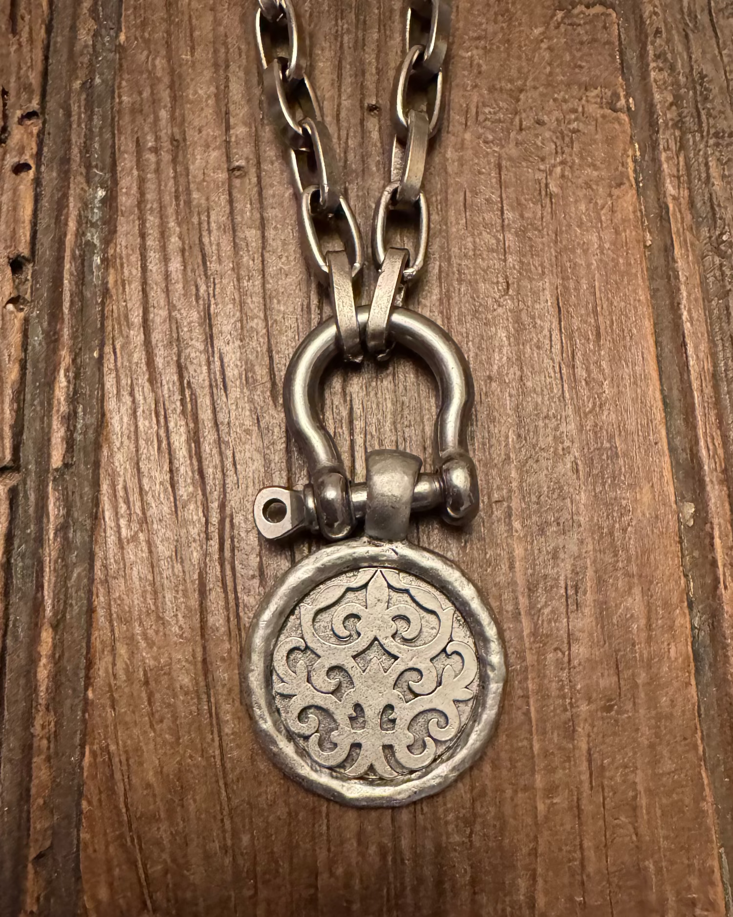Silver padlock-shaped pendant on a chain against a wooden background