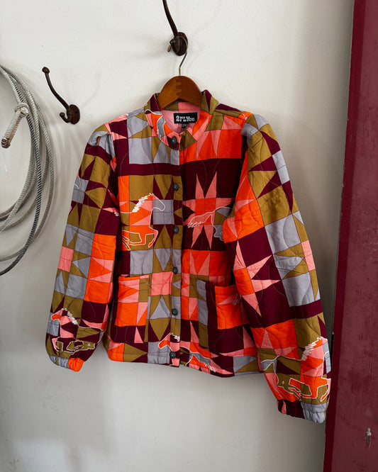 A vintage long-sleeve button-up shirt jacket with a colorful geometric patchwork pattern, hanging on a wooden hanger against a white wall.