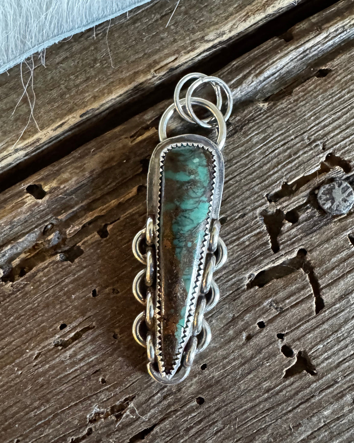 A handmade sterling silver pendant featuring a central turquoise stone, displayed on a rustic dark wood surface.