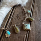 A sterling silver chain bracelet featuring multiple turquoise and green stone charms, displayed on a rustic dark wood surface next to a white faux fur accent.