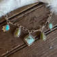 A silver chain bracelet with multiple turquoise and green stone charms, styled on a rustic dark wood background next to a white faux fur trim.