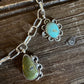 Silver chain necklace with two turquoise and green stone pendants on a dark wooden surface.