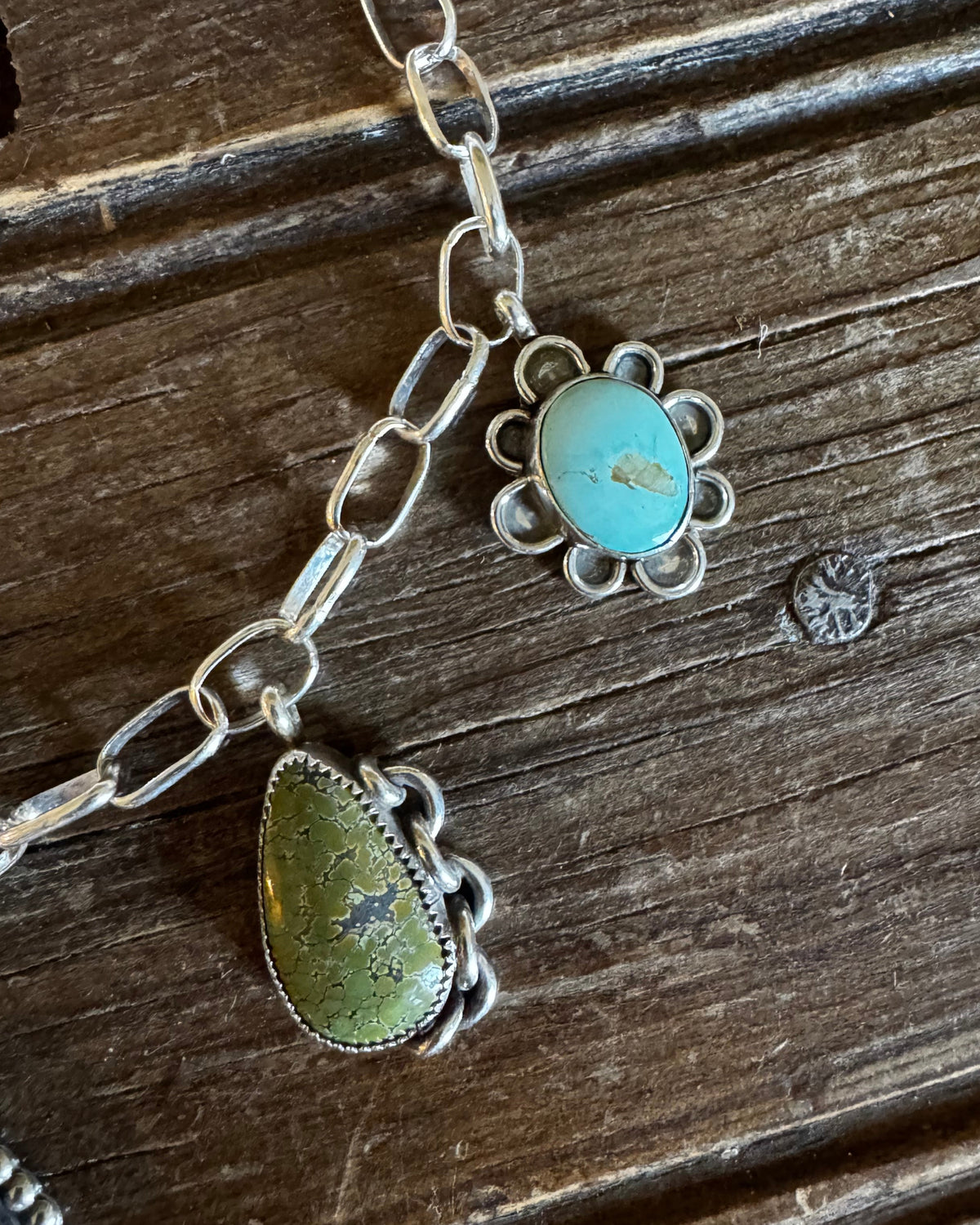 Silver chain necklace with two turquoise and green stone pendants on a dark wooden surface.