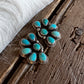 A pair of silver-toned floral stud earrings with turquoise stones, resting on a rustic dark wood surface next to a white faux fur trim.