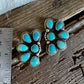 Two silver-toned floral turquoise stud earrings displayed on a rustic wooden surface next to a stainless steel ruler for scale.