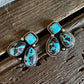A pair of silver-toned drop earrings with rectangular turquoise stones and teardrop-shaped turquoise and black marbled stones, displayed on a rustic wooden surface.