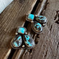 A pair of silver dangle earrings with turquoise and black marbled stones, displayed on a rustic wooden surface next to a white faux fur trim.