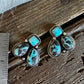 A pair of turquoise and stone drop earrings displayed on a rustic wooden surface next to a metal ruler for scale.
