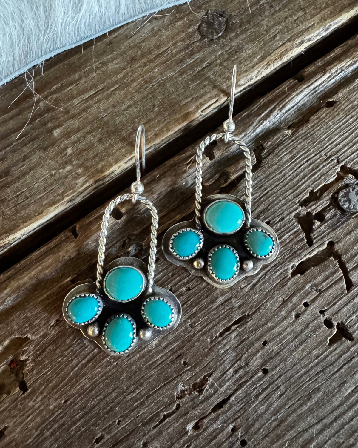 A pair of silver dangle earrings with turquoise stone clusters, displayed on a rustic dark wood surface.