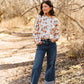 Woman standing in a forest wearing a patterned blouse and jeans.
