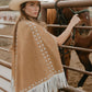 Woman wearing a brown suede leather cape standing by a fence with a horse 
