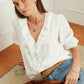 Woman wearing a white blouse and blue jeans, holding a brown bag indoors.