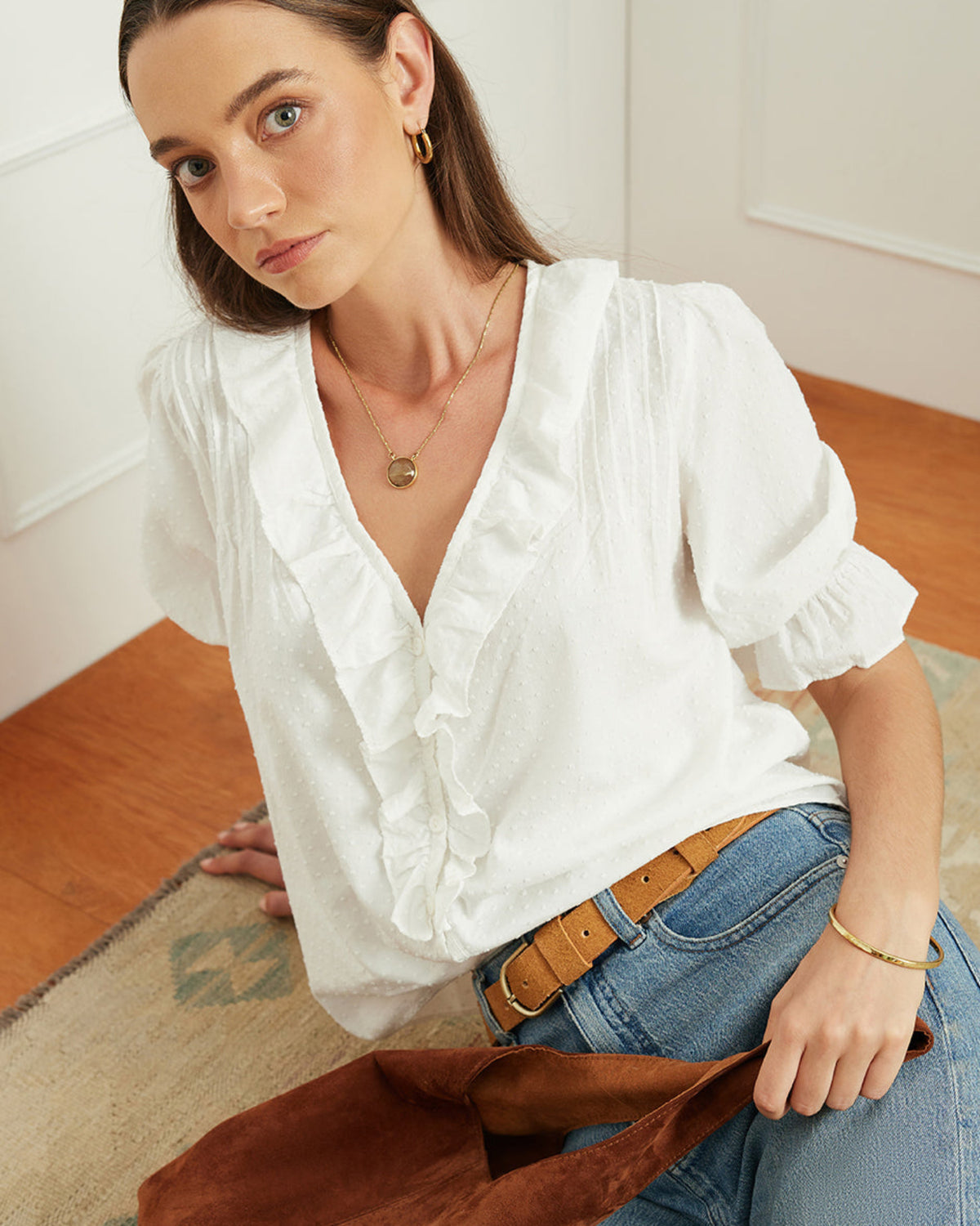 Woman wearing a white blouse and blue jeans, holding a brown bag indoors.