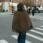 Person wearing a brown fringed cape walking on a city street.
