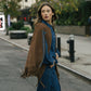 Woman walking on a city street wearing a brown fringed jacket and blue outfit.