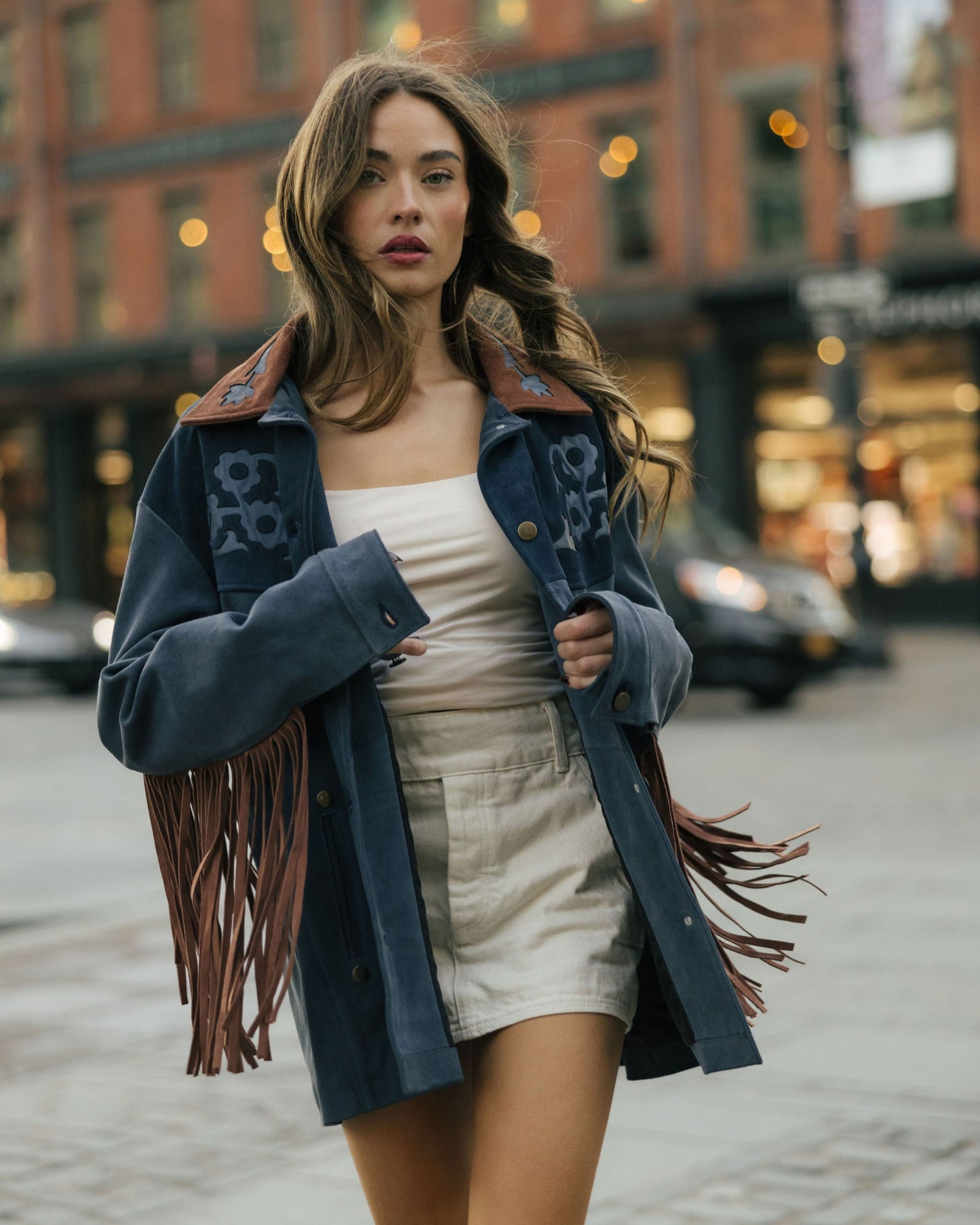 Woman in a stylish outfit with a fringed jacket walking on a street.