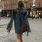 Person wearing a blue leather jacket with fringe walking on a city street.